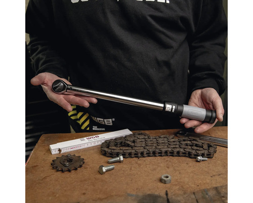 Drehmomentschlüssel aus Metall mit verstellbarem Griff, präsentiert von einer Person über einer Werkbank mit Kette und Werkzeugen.