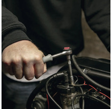 Main utilisant une petite clé à cliquet avec une poignée grise sur une pièce de moteur.