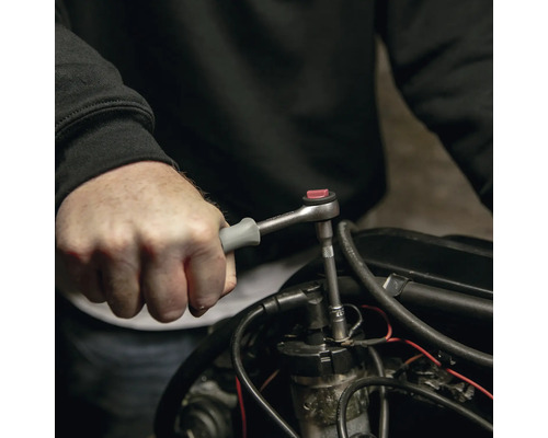 Main utilisant une petite clé à cliquet avec une poignée grise sur une pièce de moteur.