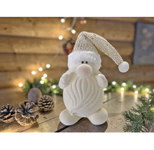 Dekorativer Weihnachtswichtel in Weiß mit Strickmütze auf Holzgrund mit Tannenzapfen und Lichterkette.