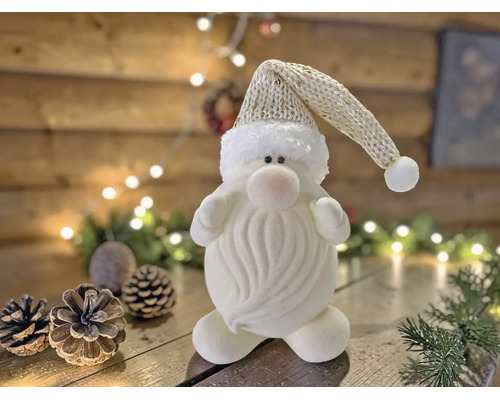 Dekorativer Weihnachtswichtel in Weiß mit Strickmütze auf Holzgrund mit Tannenzapfen und Lichterkette.