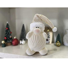 Weiße Plüschfigur eines Weihnachtsmanns mit Bart und langer Strickmütze auf einem Regal neben kleinen Tannenbäumen und Weihnachtsschmuck.