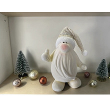 Kleine weiße Weihnachtsmann-Figur mit Daumen nach oben, Strickmütze, kleinen Tannenbäumen und Weihnachtskugeln auf einer Ablage.