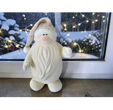 Weihnachtsmann-Dekofigur mit langem Bart und glitzernder Mütze auf Fensterbank vor verschneitem Hintergrund mit Lichterkette.