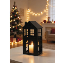 Lanterne noire en forme de maison avec bougie allumée dans un salon décoré pour Noël avec sapin et guirlande lumineuse.