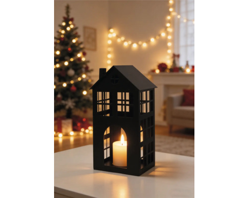 Lanterne noire en forme de maison avec bougie allumée dans un salon décoré pour Noël avec sapin et guirlande lumineuse.