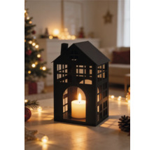 Lanterne noire en métal en forme de maison avec bougie dans un salon lumineux avec sapin de Noël et guirlandes.