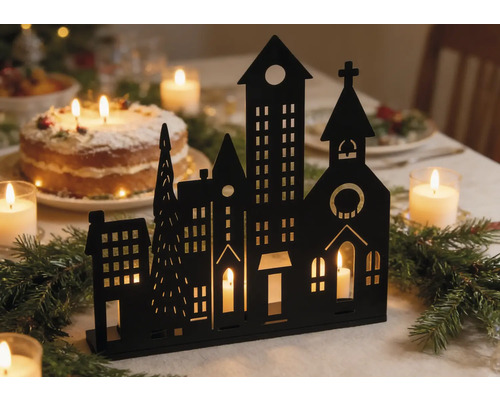Schwarze Silhouette einer Winterstadt als Kerzenhalter auf einem festlich geschmückten Tisch mit Tannenzweigen und Kerzen.