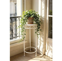 Hoher weißer Blumenhocker aus Metall mit runder Abstellfläche und Ornamenten, dekoriert mit einer Efeupflanze in einem hellen Raum.