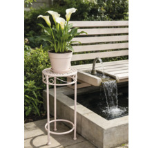 Hoher Blumenständer aus Metall mit dekorativen Verzierungen neben einer Gartenbank und einem Springbrunnen im Garten.