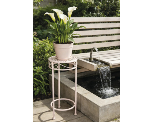 Hoher Blumenständer aus Metall mit dekorativen Verzierungen neben einer Gartenbank und einem Springbrunnen im Garten.