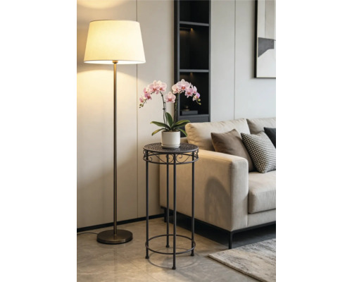 Moderner Pflanzenständer aus dunklem Metall mit einer rosa Orchidee in einem hellen Wohnzimmer neben einem beigen Sofa und einer Stehlampe.