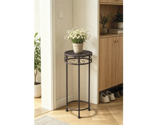 Hoher Blumenständer aus dunklem Metall mit dekorativem Muster, bestückt mit weißen Blumen in einem hellen Raum neben einem Holzschrank.