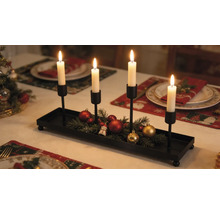 Adventskerzenhalter aus schwarzem Metall mit vier Kerzenhaltern, dekoriert mit Tannengrün und Weihnachtskugeln auf einem festlich gedeckten Tisch.