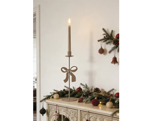 Schlanker Metallkerzenständer mit Schleife und brennender Kerze auf einer Kommode mit Weihnachtsdekoration aus Tannenzweigen und Kugeln.