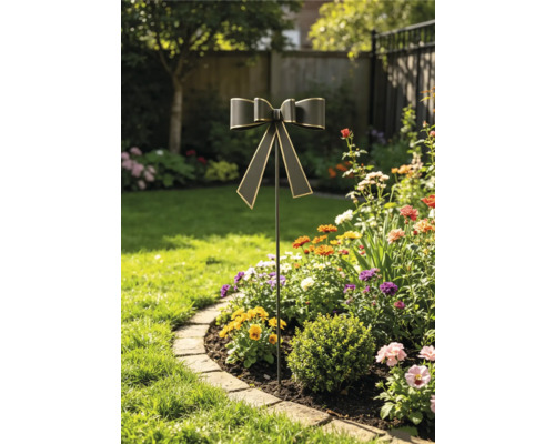 Dekorativer Gartenstecker aus Metall mit Schleife in einem sonnigen Blumenbeet mit bunten Pflanzen und angrenzendem Rasen.