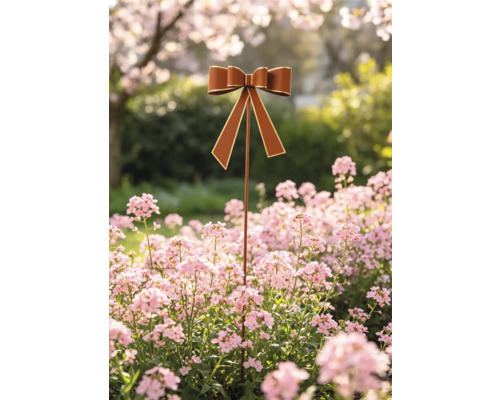 Dekorativer Gartenstab mit brauner Schleife und goldenem Rand in einem Blumenbeet mit rosa Blüten.