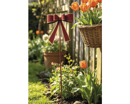 Gartenstecker mit roter Schleife und Goldrand in einem sonnigen Garten mit Tulpen und einem geflochtenen Korb.