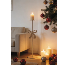 Hoher Kerzenständer mit Schleife in einer weihnachtlich dekorierten Wohnzimmerecke neben einem Sofa und beleuchteten Stumpenkerzen.