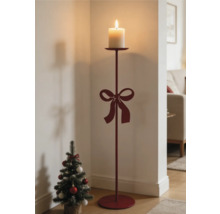 Roter Bodenkerzenständer aus Metall mit Schleife und brennender Stumpenkerze neben einem kleinen Weihnachtsbaum in einem hellen Raum.