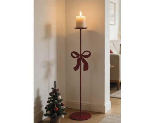 Roter Bodenkerzenständer aus Metall mit Schleife und brennender Stumpenkerze neben einem kleinen Weihnachtsbaum in einem hellen Raum.