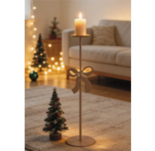 Hoher Metall-Kerzenständer mit Schleifendekor und brennender Stumpenkerze in einem hellen Wohnzimmer mit Weihnachtsdekoration.