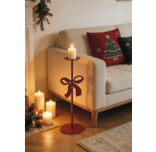 Hoher Bodenkerzenständer aus Metall mit Schleife in einem weihnachtlich dekorierten Wohnzimmer mit Sofa und brennenden Kerzen.