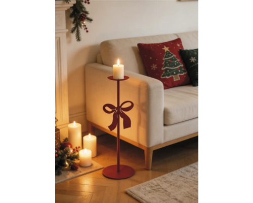 Hoher Bodenkerzenständer aus Metall mit Schleife in einem weihnachtlich dekorierten Wohnzimmer mit Sofa und brennenden Kerzen.