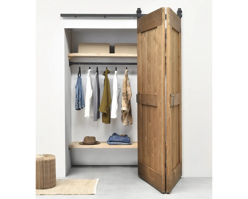 Porte coulissante pliante en bois de style grange devant un dressing organisé avec un système de rails noirs.