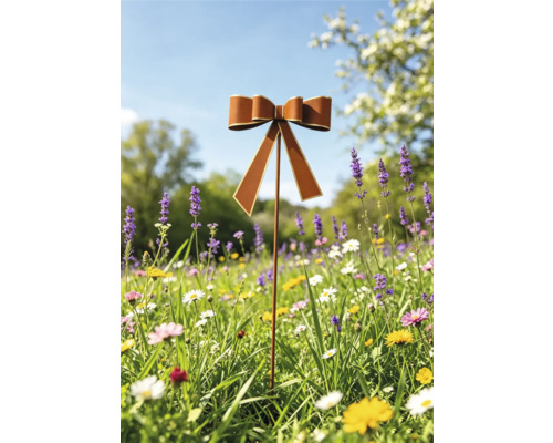 Gartenstecker aus Metall mit dekorativer Schleife in Rostoptik auf einer Blumenwiese.