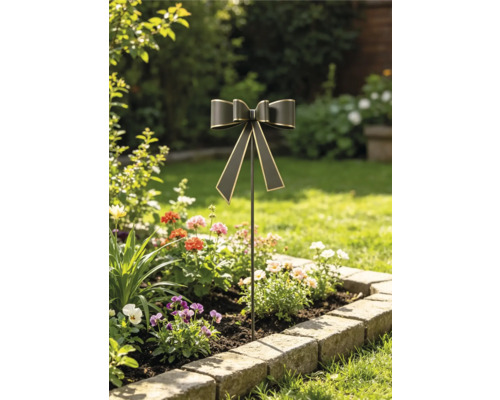 Gartenstecker in Form einer Schleife mit Goldkanten in einem bepflanzten Blumenbeet mit Natursteineinfassung.