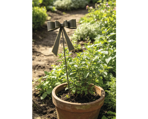 Gartenstecker mit einer Schleife in einem bepflanzten Terrakotta-Topf in einer grünen Gartenumgebung.