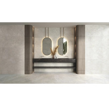Salle de bains moderne avec carrelage mural aspect pierre claire, double vasque aspect marbre noir et deux miroirs ovales rétroéclairés.
