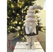 Festliche Weihnachtsdekoration mit einem großen Plüschwichtel mit Bart und spitzer Mütze vor einem beleuchteten Weihnachtsbaum.