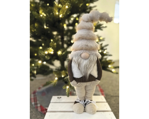 Festliche Weihnachtsdekoration mit einem großen Plüschwichtel mit Bart und spitzer Mütze vor einem beleuchteten Weihnachtsbaum.