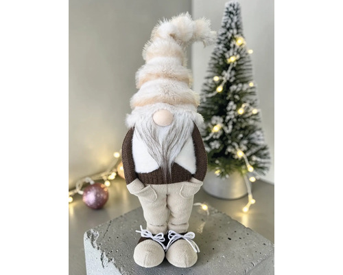 Dekorativer Wichtel mit Plüschmütze, Bart und Textilkleidung neben einem kleinen Weihnachtsbaum.