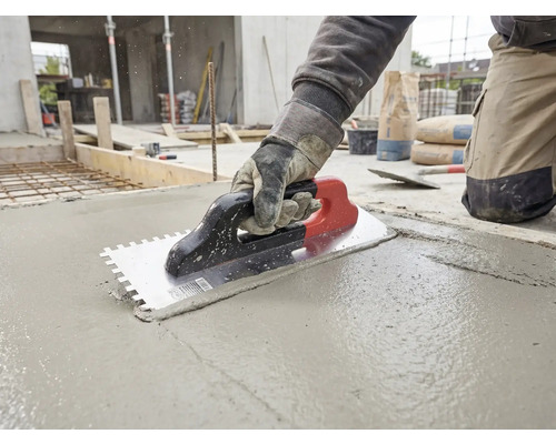 Un artisan utilise une truelle dentelée pour lisser du béton frais sur un chantier.