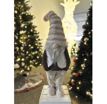 Dekorative Weihnachtswichtel-Figur mit langer Mütze und grauem Bart, stehend zwischen beleuchteten Weihnachtsbäumen.