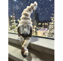 Dekofigur Wichtel mit flauschiger Mütze und weißem Bart, sitzend auf einer Fensterbank vor winterlicher Kulisse mit Lichtern.