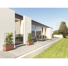 Tomatenpflanzen in Kunststoff-Pflanzgefäßen mit Rankgittern auf einer modernen Terrasse mit Gartenmöbeln und angrenzender Rasenfläche.