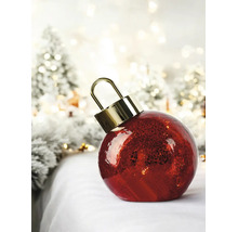 Grande boule de Noël rouge à surface texturée et attache dorée dans un décor hivernal illuminé.