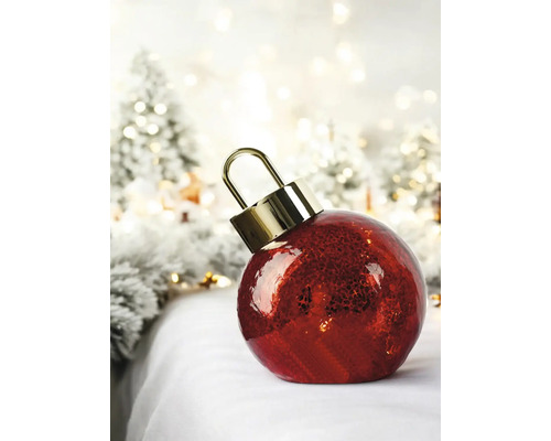 Grande boule de Noël rouge à surface texturée et attache dorée dans un décor hivernal illuminé.