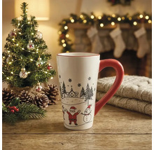 Weisse Keramiktasse mit rotem Henkel, Weihnachtsmann und Schneemann auf Holztisch vor einem beleuchteten Tannenbaum und Kamin.