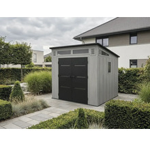 Abri de jardin moderne avec parois grises aspect bois, doubles portes noires et fenêtres, situé sur des dalles en pierre dans un jardin.