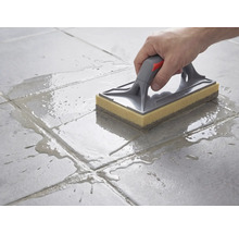 Nettoyage de carreaux de sol avec une taloche éponge à poignée grise et éponge jaune après le jointoiement.