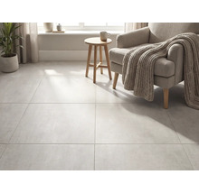 Carreaux de sol grand format aspect béton dans un salon lumineux avec fauteuil, couverture en tricot et table d appoint en bois.