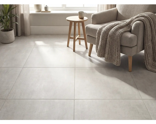 Carreaux de sol grand format aspect béton dans un salon lumineux avec fauteuil, couverture en tricot et table d appoint en bois.