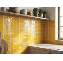 Crédence de cuisine avec carreaux muraux carrés jaunes brillants, une étagère en bois avec des bols et des herbes et un plan de travail.