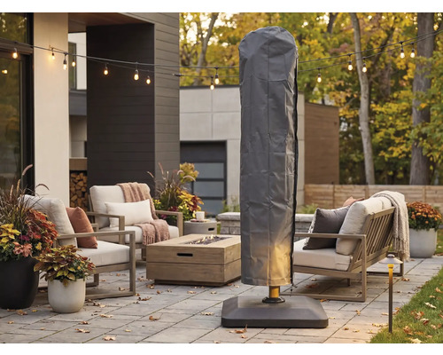 Housse de protection grise pour parasol déporté sur une terrasse moderne avec salon de jardin, table de foyer et guirlande lumineuse.