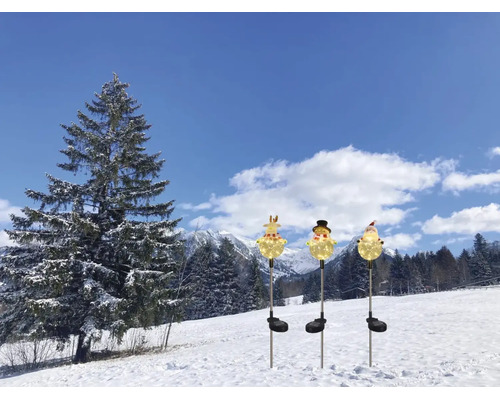 Drei solarbetriebene Gartenstecker in Form von Rentier, Schneemann und Weihnachtsmann, leuchtend in einer verschneiten Winterlandschaft.